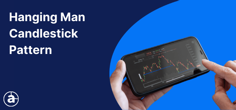 A hand holding a smart phone with a trading platform open on the screen, white text reads: "Hanging Man Candlestick Pattern".