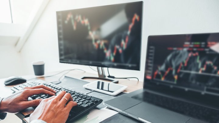Mano che sta digitando al computer con davanti un grafico di trading a candele che mostra il breakout trading.