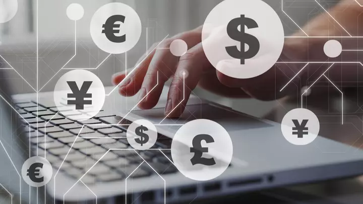 Mano sulla tastiera di un portatile con rappresentati simboli di valute quali dollaro, yen, euro per indicare il carry trade.