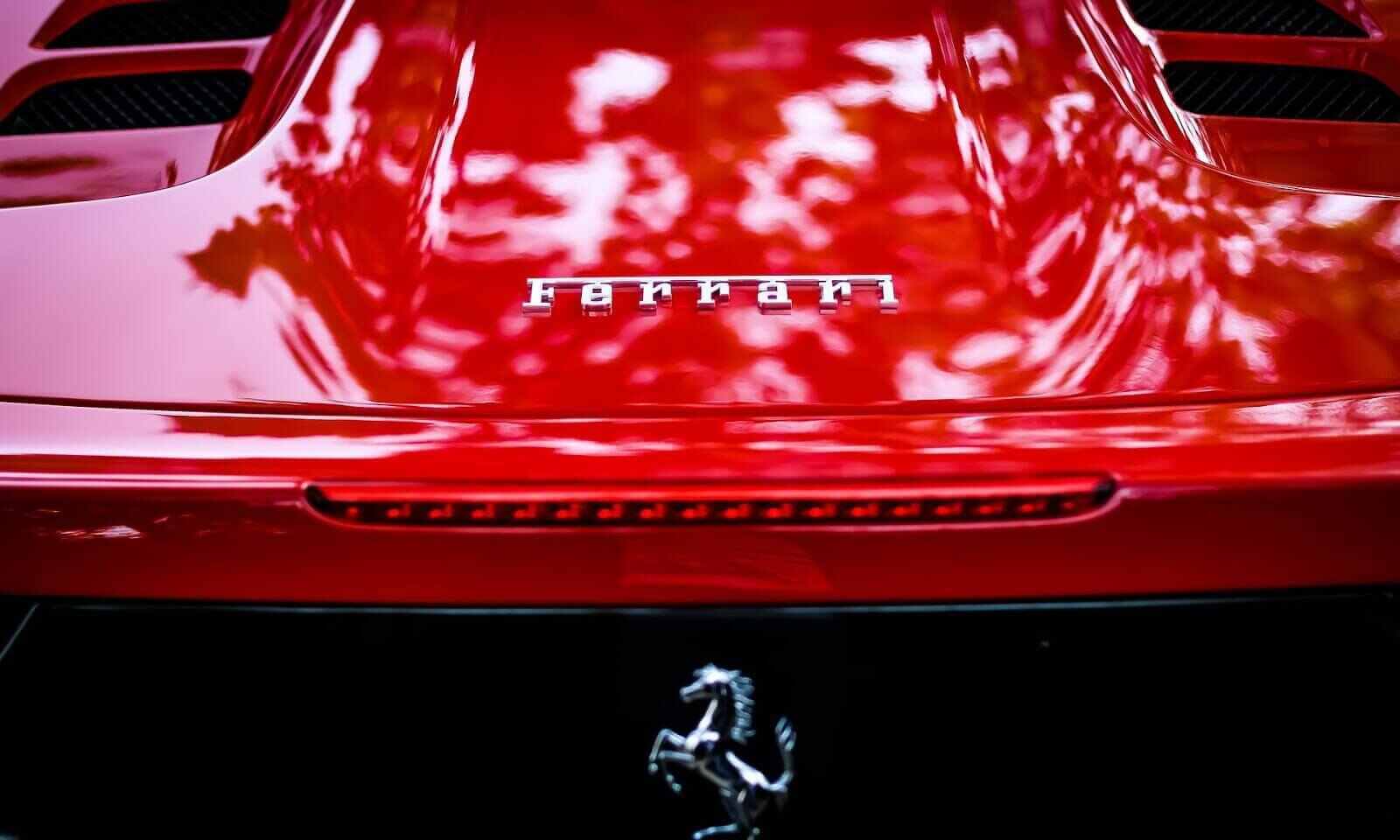 Parte retro di un auto rossa con logo Ferrari e quello di un cavallino rampante, a indicare comprare azioni Ferrari.