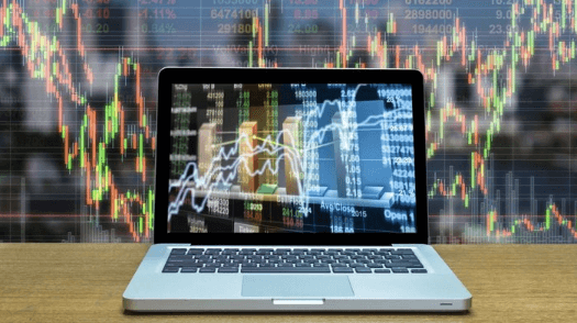 Sfondo di un grafico trading candlestick con pc su un desk, che mostra grafico a linee e numeri, per indicare Metatrader 5 come funziona.