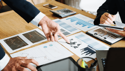 Sfondo di ufficio con fogli che rappresentano grafici di trading candlestick e a colonne, a indicare il piano di trading.