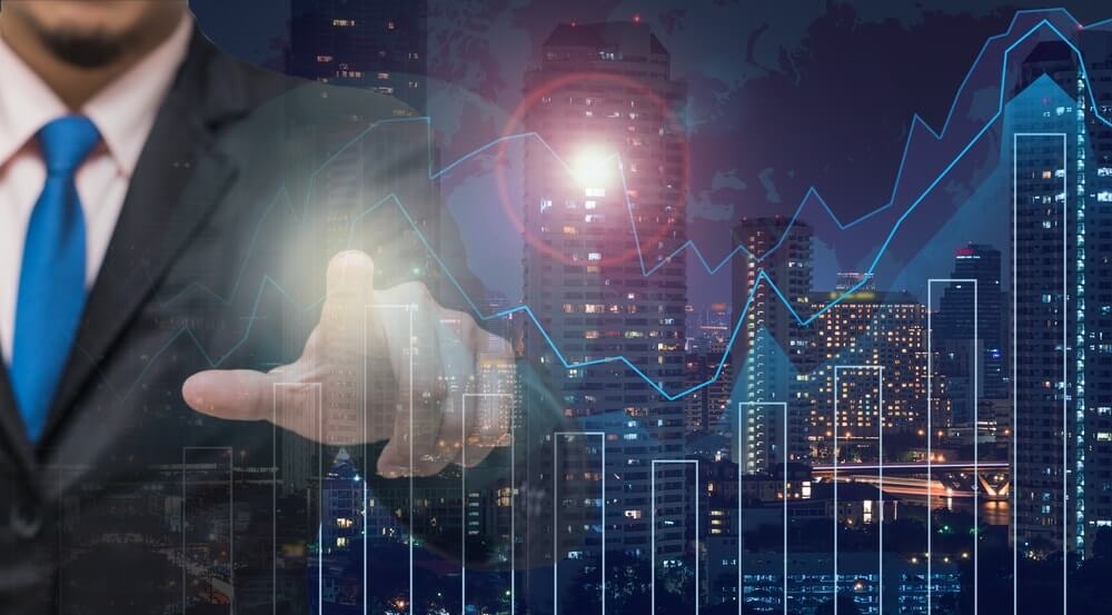 Persona che indica con un dito della mano dei grafici di trading, uno a colonne e uno a linee e che potrebbe indicare il vps trading o server privato virtuale